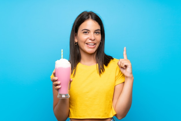 Ragazza con il frappé della fragola sopra la parete isolata che indica su una grande idea