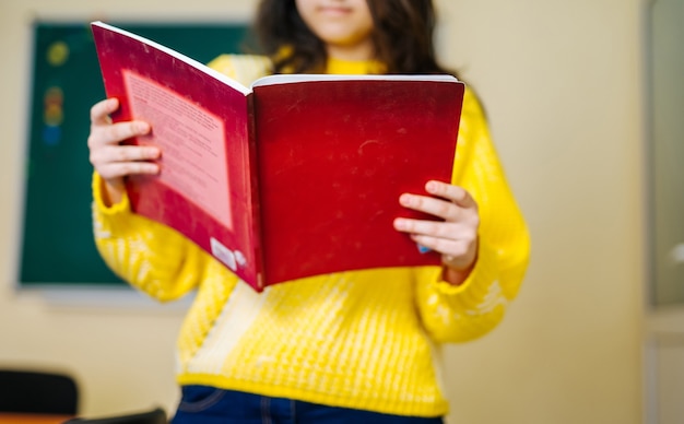 Ragazza con il libro di testo rosso nelle mani. Concetto di scuola. maglione giallo. Studente universitario.