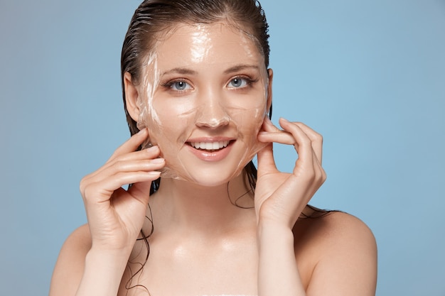 Ragazza con il sorriso sul viso e capelli bagnati che rimuove la maschera trasparente facciale