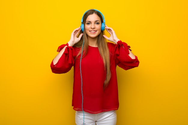 Ragazza con il vestito rosso sopra la parete gialla che ascolta la musica con le cuffie