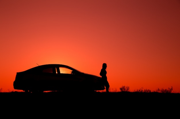 Ragazza con l'automobile sul cielo di tramonto