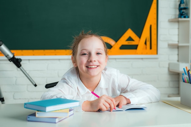 Ragazza con l'espressione del viso felice vicino alla scrivania con materiale scolastico