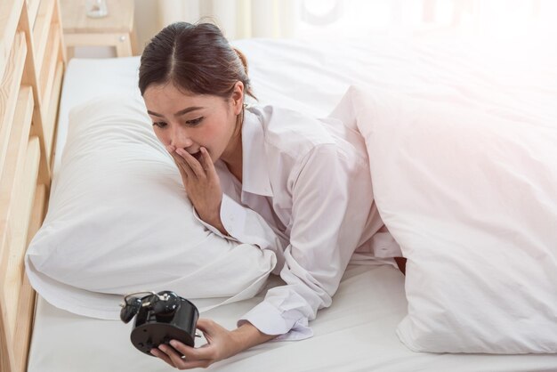 Ragazza con la mano che tocca la sveglia sul letto per svegliarsi