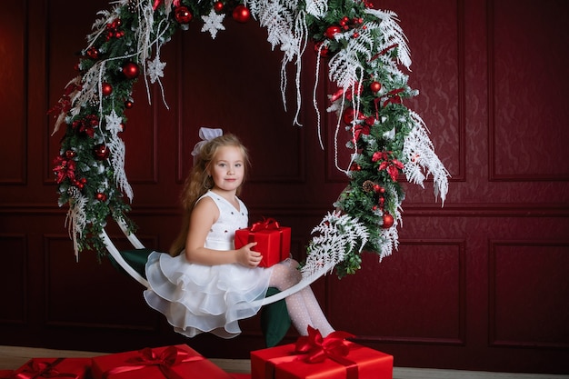 Ragazza con la scatola rossa. Regalo di Natale. Teen si siede sull'altalena ad arco con ghirlande decorative di Capodanno, rami di abete rosso, palline e ghirlande.