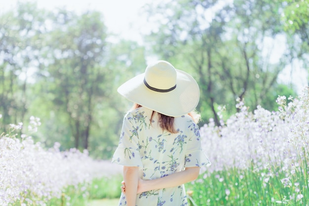 Ragazza con la schiena e cappello di paglia in un campo di fiori, donna asiatica felice