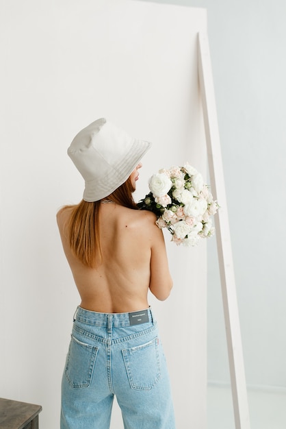 Ragazza con la schiena nuda in blue jeans e un cappello bianco con un mazzo di fiori