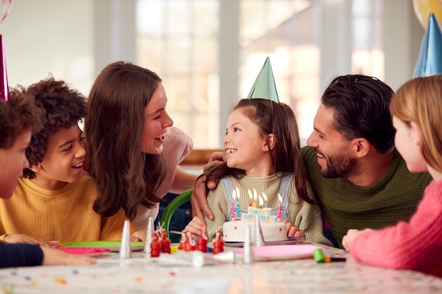 Ragazza con le candele sulla torta di compleanno alla festa a sorpresa con i genitori e gli amici a casa