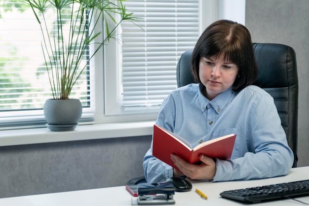 Ragazza con libro sul posto di lavoro. Il capo donna legge al lavoro durante la pausa pranzo.