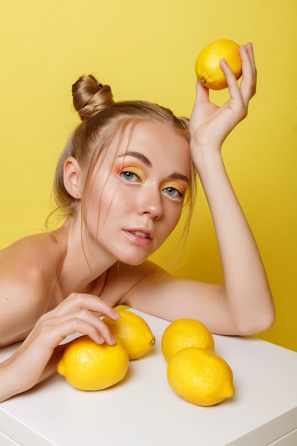 Ragazza con limoni su una parete gialla con trucco luminoso. umore estivo