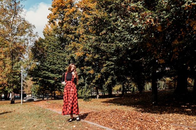 Ragazza con lunghi capelli castani in autunno parco Ragazza con abito lungo rosso scozzese