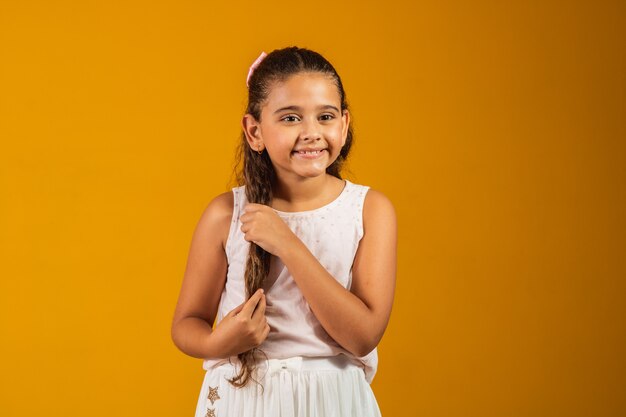 Ragazza con lunghi capelli ondulati sani. Bellezza, aspetto, acconciatura. Modello bambino con sorriso sul viso carino su sfondo giallo. Bambino felice, concetto di infanzia. Gioventù, cura e salute.