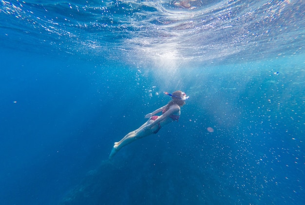 Ragazza con maschera e boccaglio si tuffa in mare con coralli e pesci