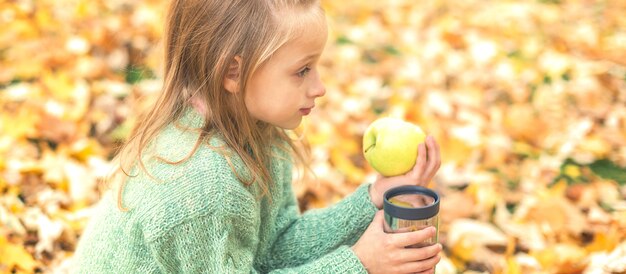 Ragazza con mela e bevanda nel parco autunnale