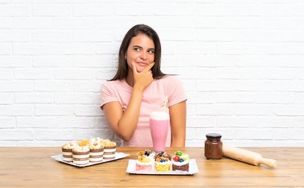 Ragazza con molte mini torte differenti che pensa un'idea