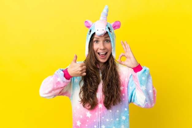 Ragazza con pigiama unicorno su sfondo isolato che mostra segno ok e gesto pollice in su