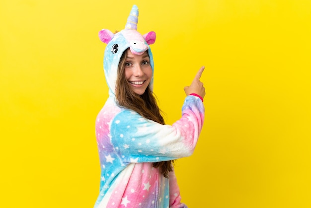 Ragazza con pigiama unicorno su sfondo isolato che punta indietro