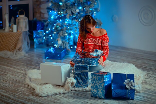 ragazza con regali di natale ragazza adulta / giovane adulta, modella all'interno del nuovo anno, disimballa i regali di natale nel pacchetto