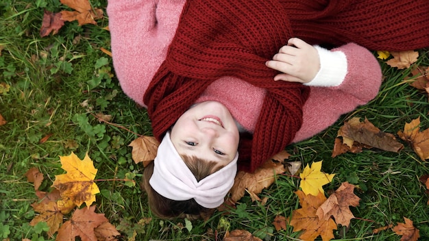 Ragazza con sciarpa rossa sorridente sdraiata sull'erba con foglie di acero