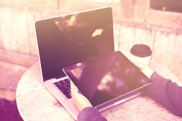 Ragazza con tavoletta digitale caffè per andare e laptop sull'effetto foto di instagram tavolo in legno