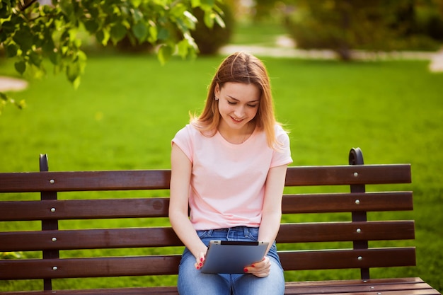 Ragazza con tavoletta seduta su una panchina nel parco