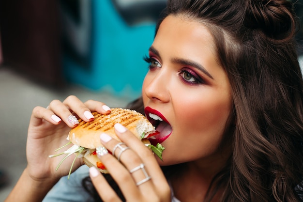 Ragazza con trucco luminoso prendendo un boccone di hamburger.