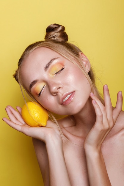 Ragazza con trucco multicolore e limone su una parete luminosa gialla