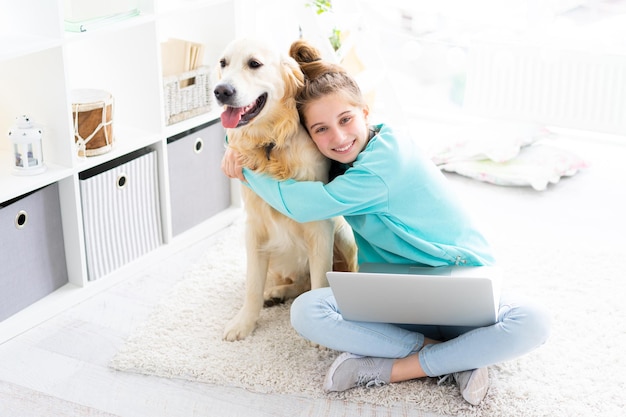 Ragazza con un bel cane con il computer portatile in una stanza luminosa