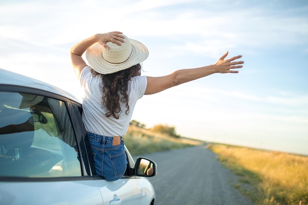 Ragazza con un cappello che sporge il corpo dal finestrino di un'auto. Concetto di libertà e avventura.