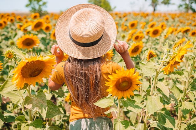 Ragazza con un cappello di paglia in piedi in un campo di girasoli