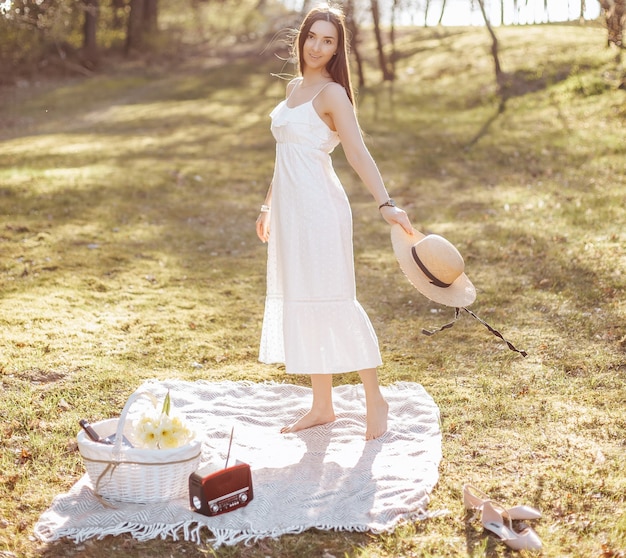 Ragazza con un cappello di paglia in primavera nel parco. Bruna con i capelli lunghi tiene un cappello su uno sfondo di natura estiva.