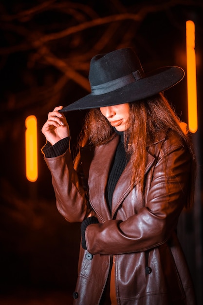 Ragazza con un cappello in un ritratto di notte su un pacco. Modello brunetta caucasica che guarda l'obbiettivo, lo stile di vita e la strada