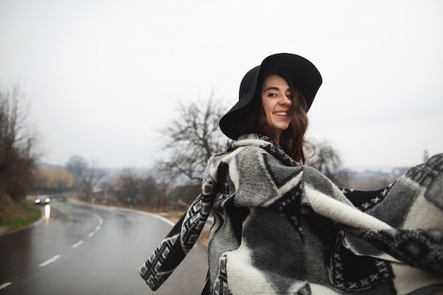 Ragazza con un cappello nero che cammina lungo la strada in una giornata piovosa