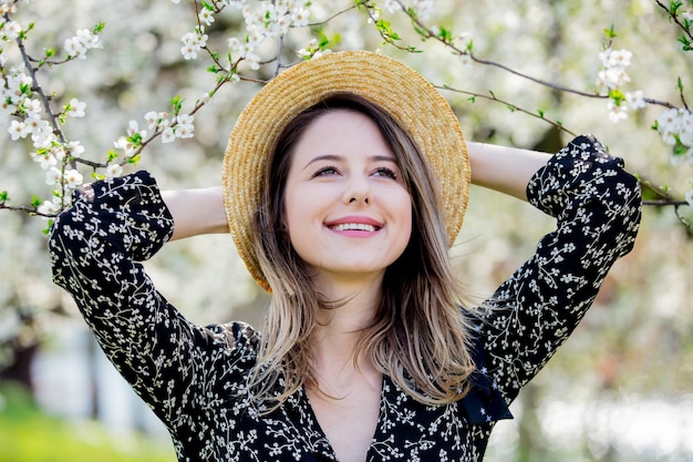 Ragazza con un cappello stare vicino a un albero in fiore nel parco. Stagione primaverile