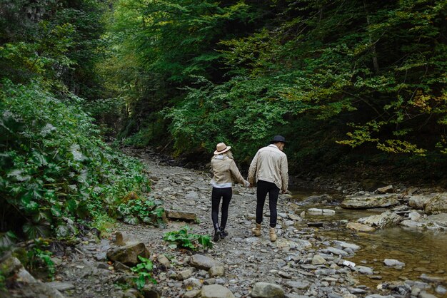 ragazza con un cappello, una giacca e un ragazzo cammina lungo una strada forestale e si tiene per mano