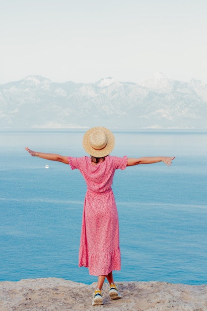 Ragazza con un cappello vicino al mare sul bordo di una scogliera con mare e montagne sullo sfondo