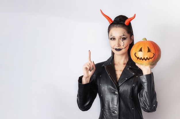 Ragazza con un cappotto di pelle e corna sulla testa con la zucca in mano