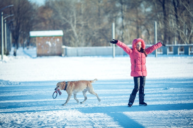 Ragazza con un cucciolo di cane Labrador che gioca in inverno all'aperto divertente