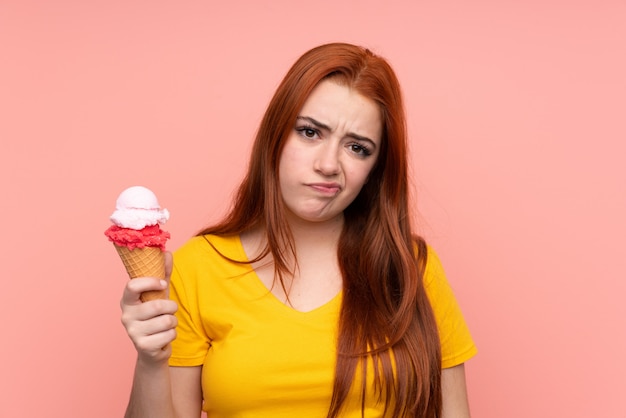 Ragazza con un gelato della cornetta sopra la parete isolata con l'espressione triste