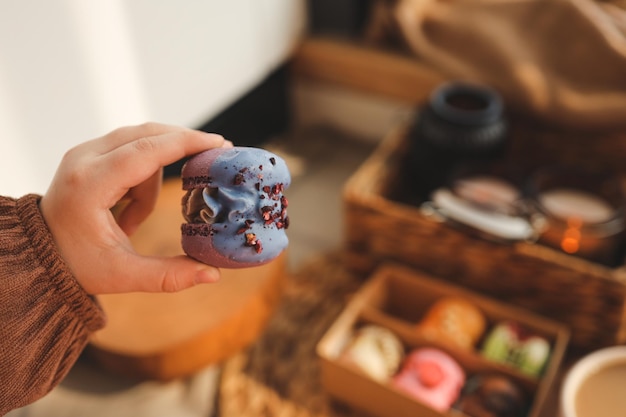 Ragazza con un macaron in mano con una scatola di macaron assortiti sullo sfondo in un'accogliente atmosfera domestica