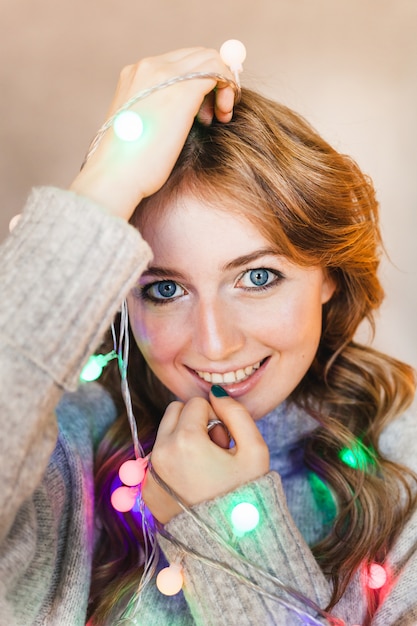 Ragazza con un maglione lungo e leggero, una giacca e una ghirlanda con luci natalizie