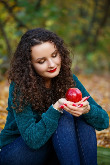 Ragazza con un maglione verde e una mela in mano nella foresta autunnale