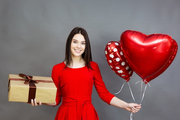 Ragazza con un regalo e palloncini. Ragazza che riceve una confezione regalo e palloncini a forma di cuore per San Valentino.