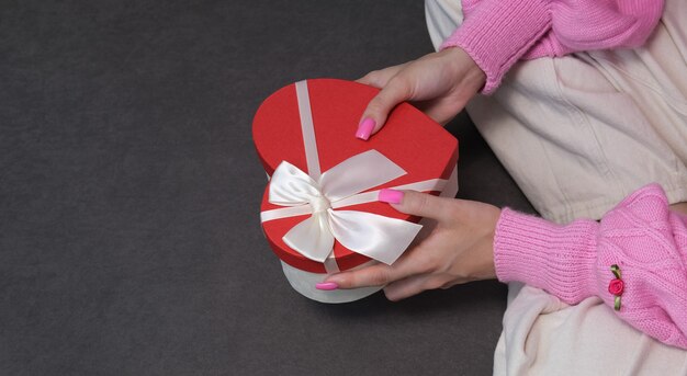 Ragazza con un regalo in una scatola rossa a forma di cuore. Sfondo scuro, messa a fuoco selettiva. Concetto venerdì nero, vacanza, compleanno, festa della donna.