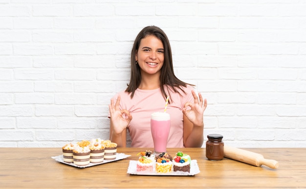 Ragazza con un sacco di diverse mini torte che mostrano un segno ok con le dita