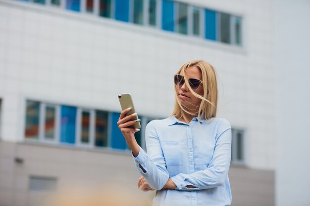 Ragazza con un telefono sul fondo della costruzione di affari. bella ragazza bionda con gli occhiali