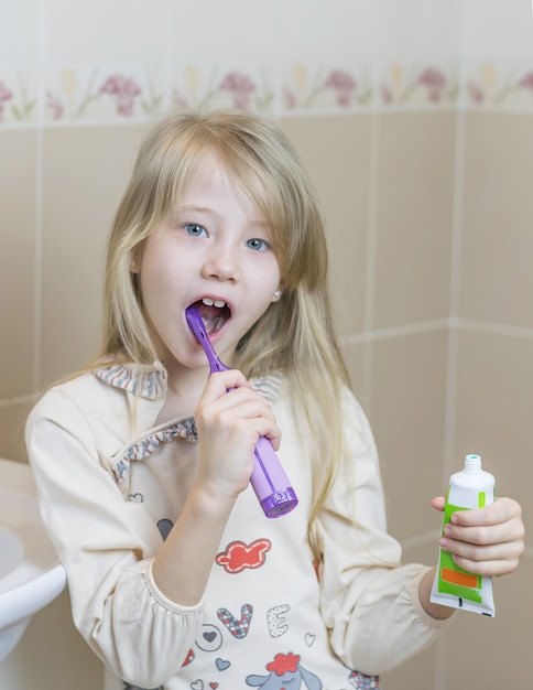 Ragazza con un tubo aperto di dentifricio e uno spazzolino elettrico.