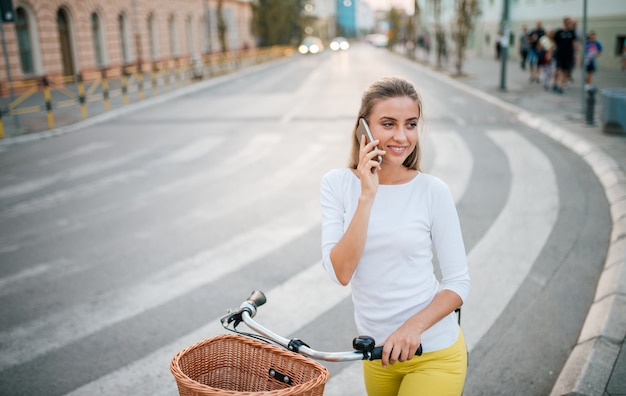 Ragazza con una bici parlando al telefono in città.