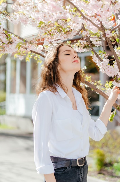 ragazza con una camicia bianca si trova vicino al sakura