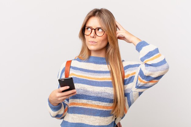 Ragazza con una cella che si sente perplessa e confusa, grattandosi la testa