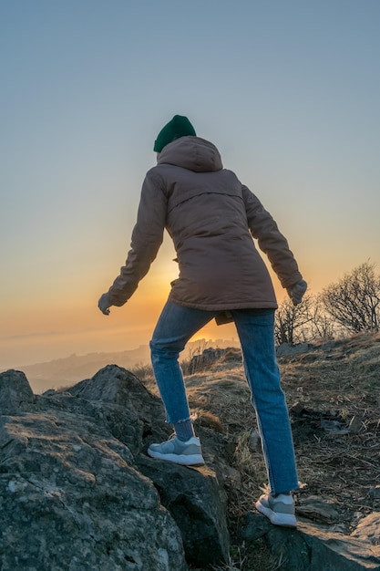 Ragazza con una giacca e un cappello sulla montagna durante il tramonto